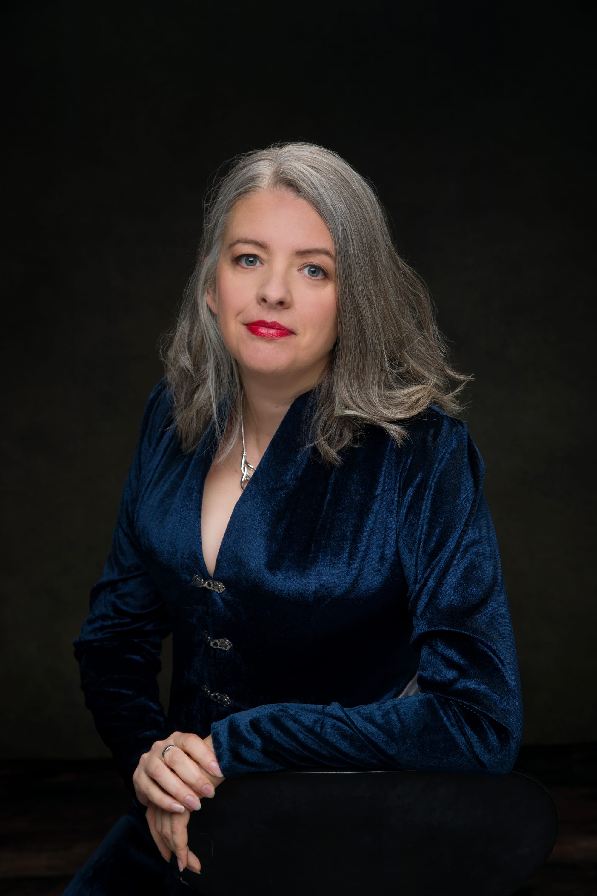 Official headshot of author Emma Newman wearing a silver and blue velvet outfit 